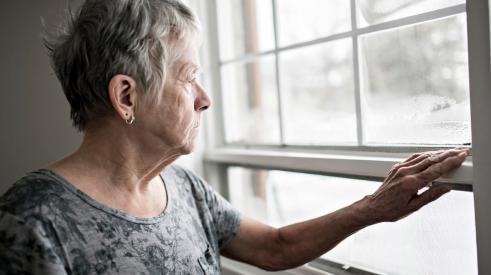 Elderly woman opening window in home and looking outside 