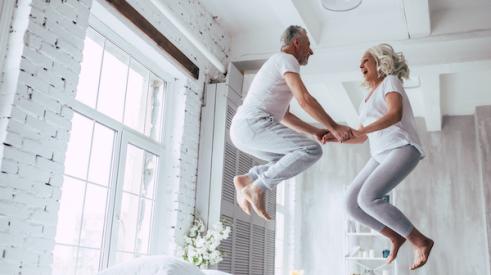 Older couple jumping on bed in apartment