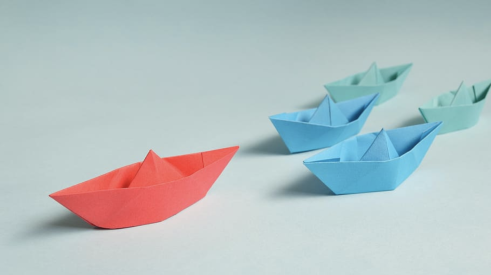 one red paper origami boat leading ahead of smaller blue origami boats 