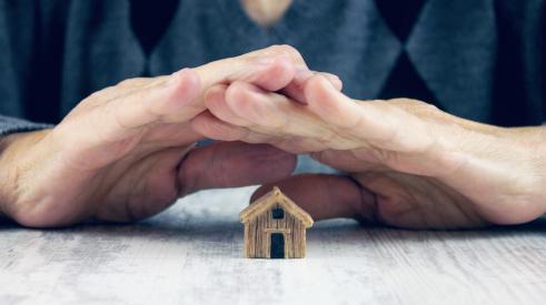 Person holding hands over small wooden house