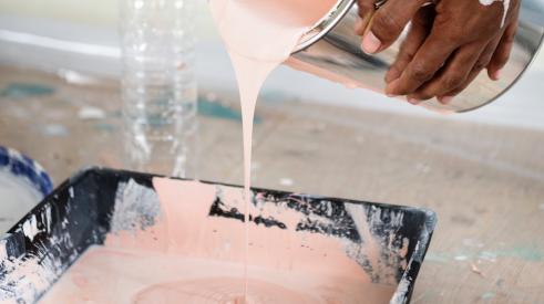 Person pouring peach paint into paint tray with roller