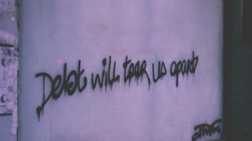 Graffiti on cement wall reads, 'debt will tear us apart'