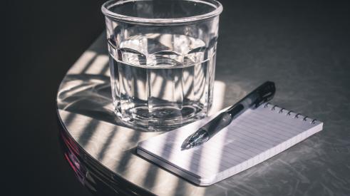Glass of water and pad with pen on table