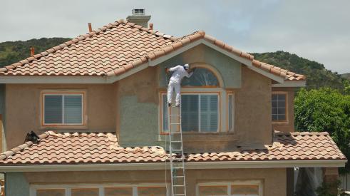 Builder on ladder adding stucco to home exterior