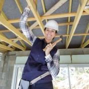 Woman standing beneath ceiling rafters in new house with hammer