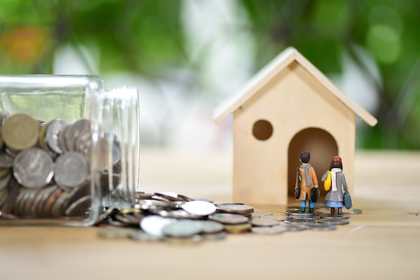 tiny home model with glass jar of coins laying on its side with coins spilling out 