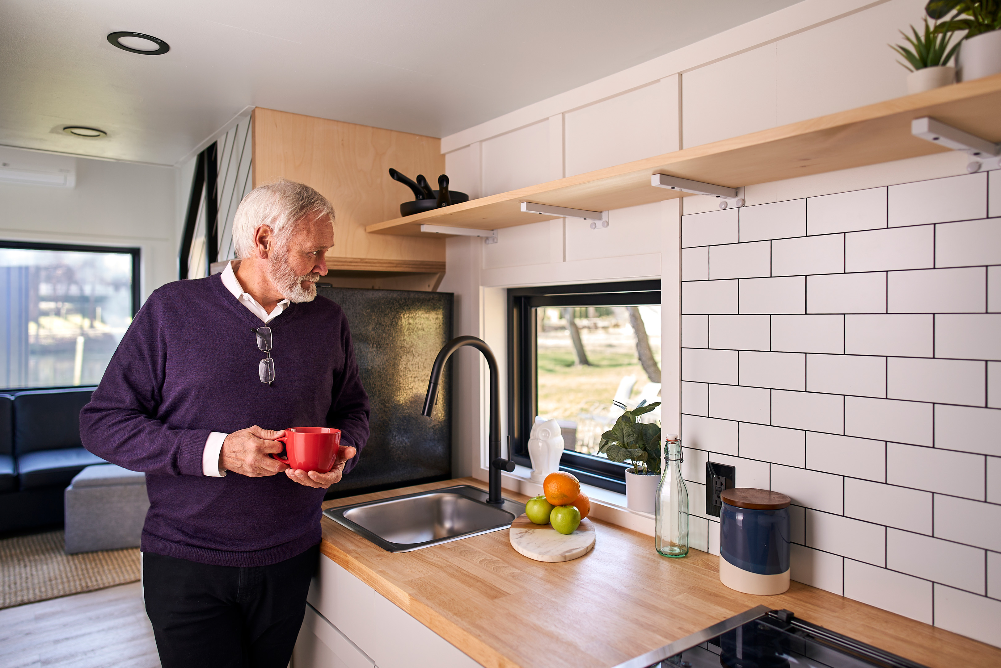 Senior drinking coffee in kitchen of Liv-Connected tiny home prototype