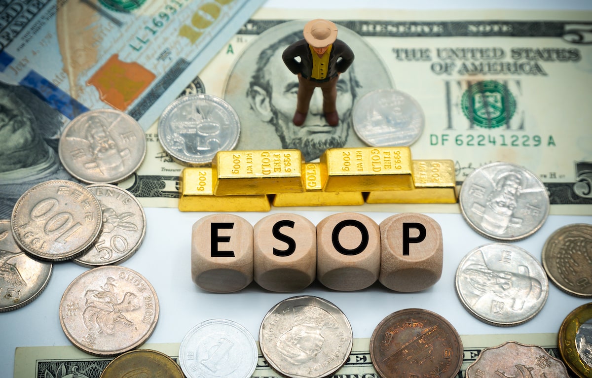 Business leader figurine standing on money in front of gold bars and letters spelling 'ESOP'