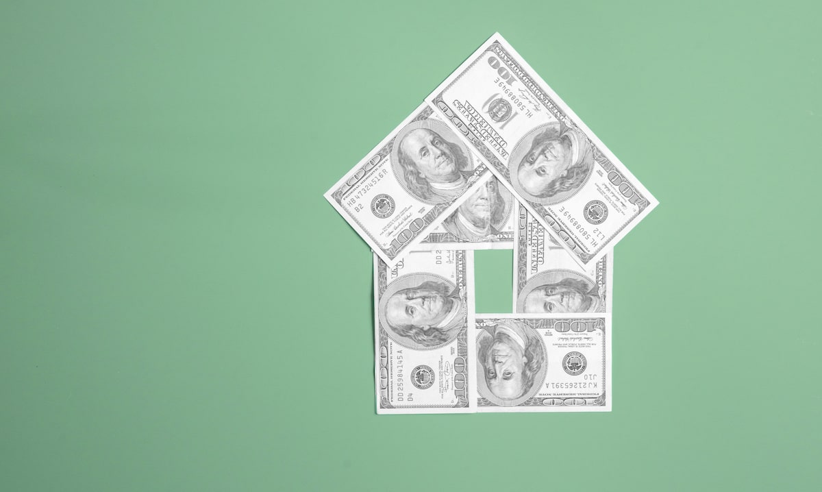 One hundred dollar bills in the shape of a house with green background