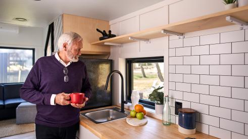 Senior drinking coffee in kitchen of Liv-Connected tiny home prototype