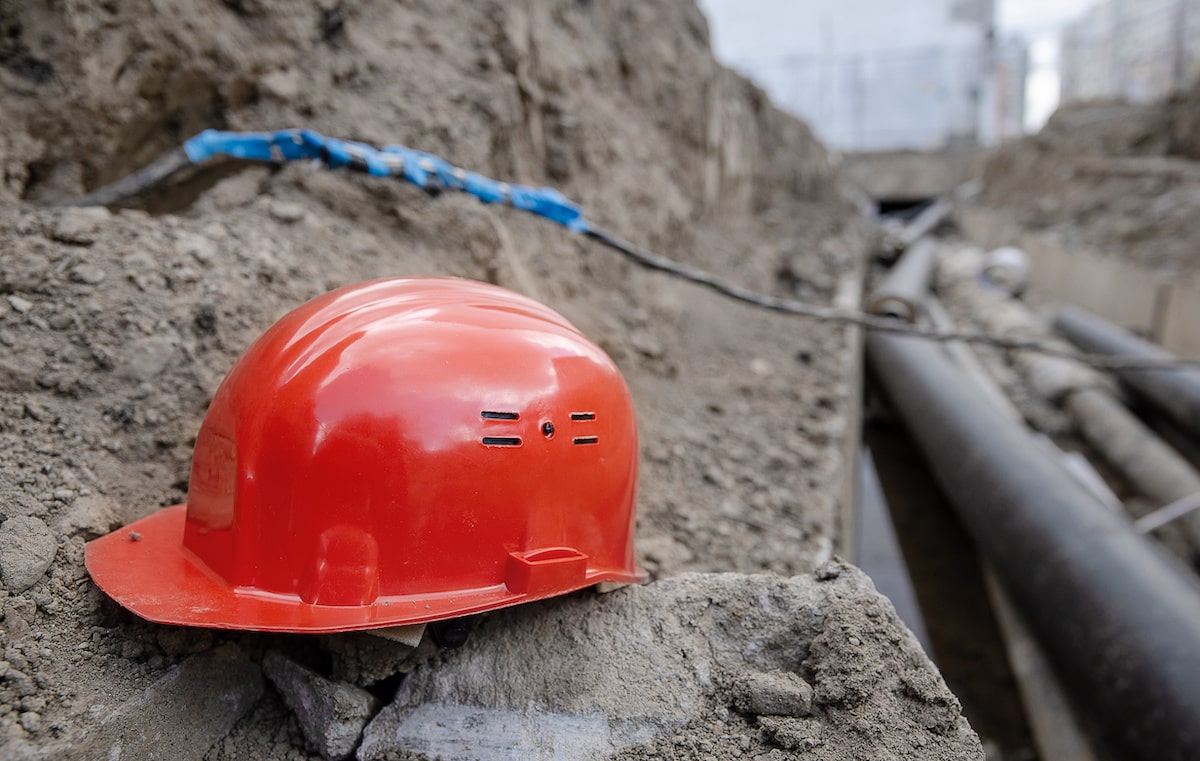 Red construction hard hat in trench 